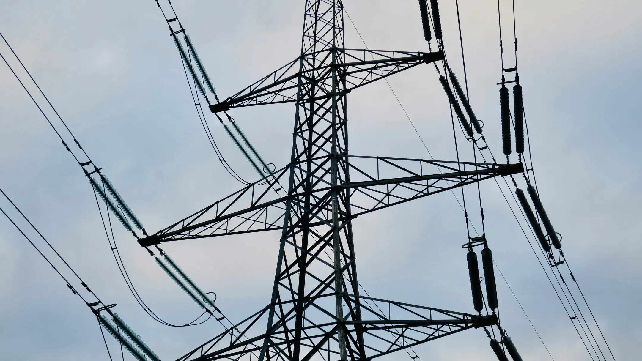 Høyspentmast med strømkabler mot en grå himmel